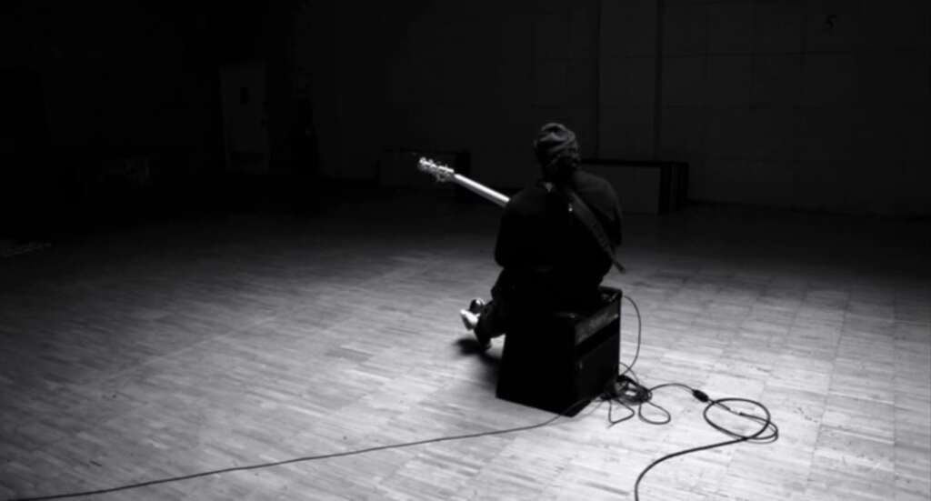 musician sitting on a speaker with his back to the camera